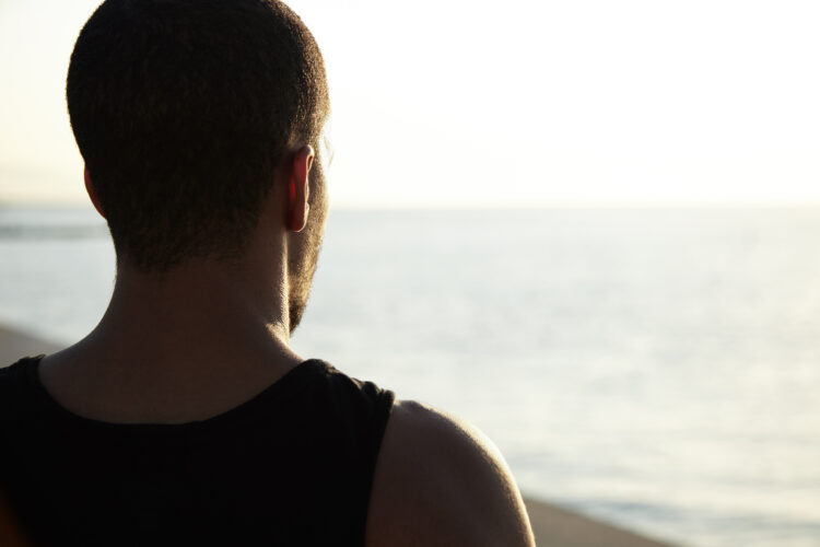 Cropped shot of African student standing by sea, watching sunrise and meditating alone before seriou